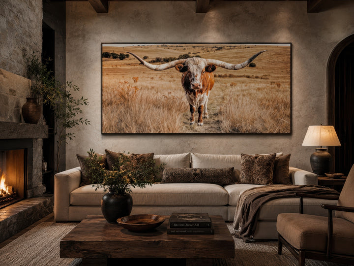Framed horizontal canvas art of a Texas Longhorn bull in a field above a modern living room sofa.