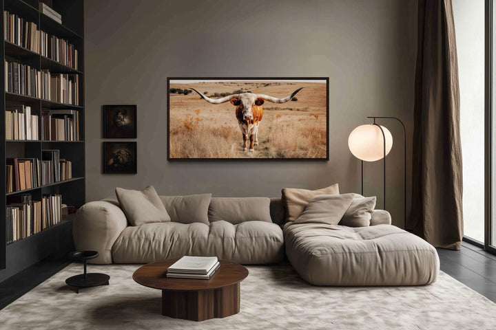 Framed canvas wall art of a Texas longhorn bull in a field, hung above a modern sectional sofa.