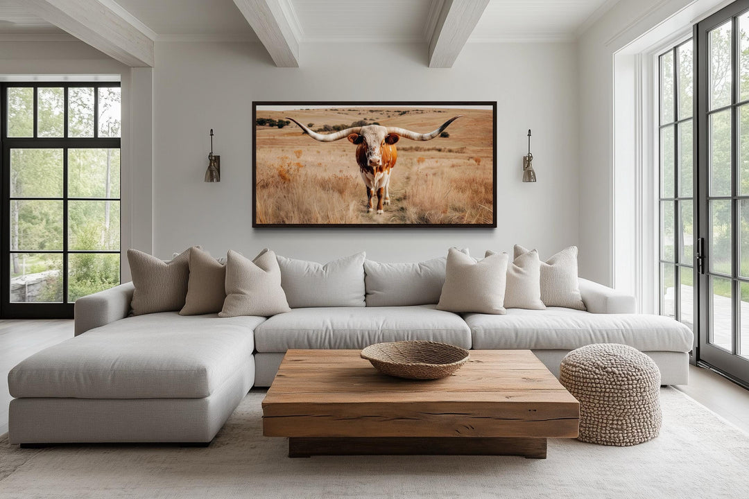 Framed canvas wall art of a Texas longhorn bull in a field, hung above a modern sectional sofa.