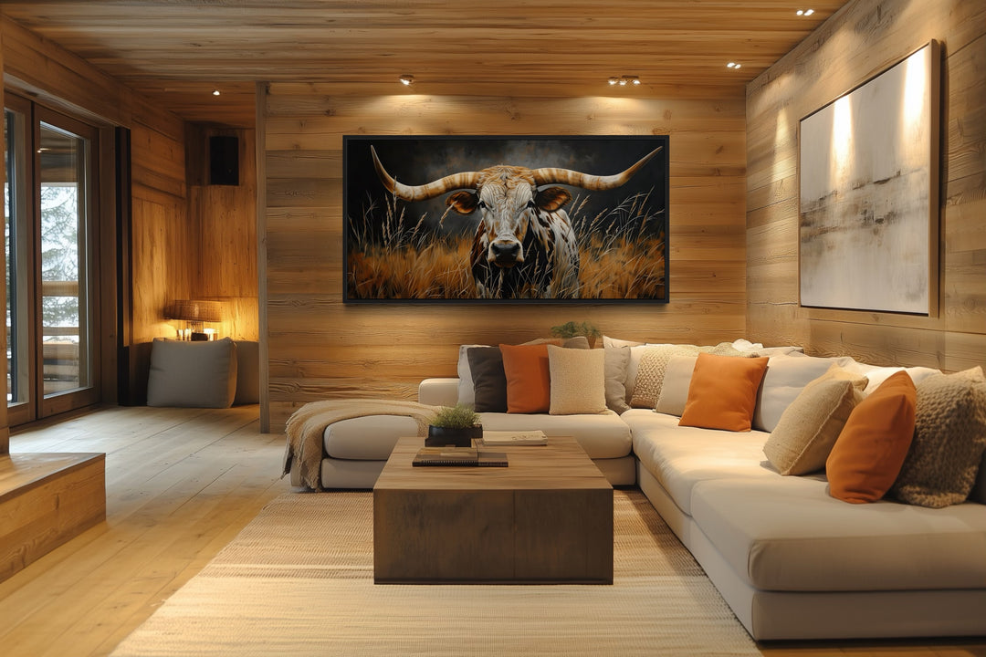 Framed canvas wall art of a Texas longhorn steer in grass, hung in a rustic wood-paneled living room.