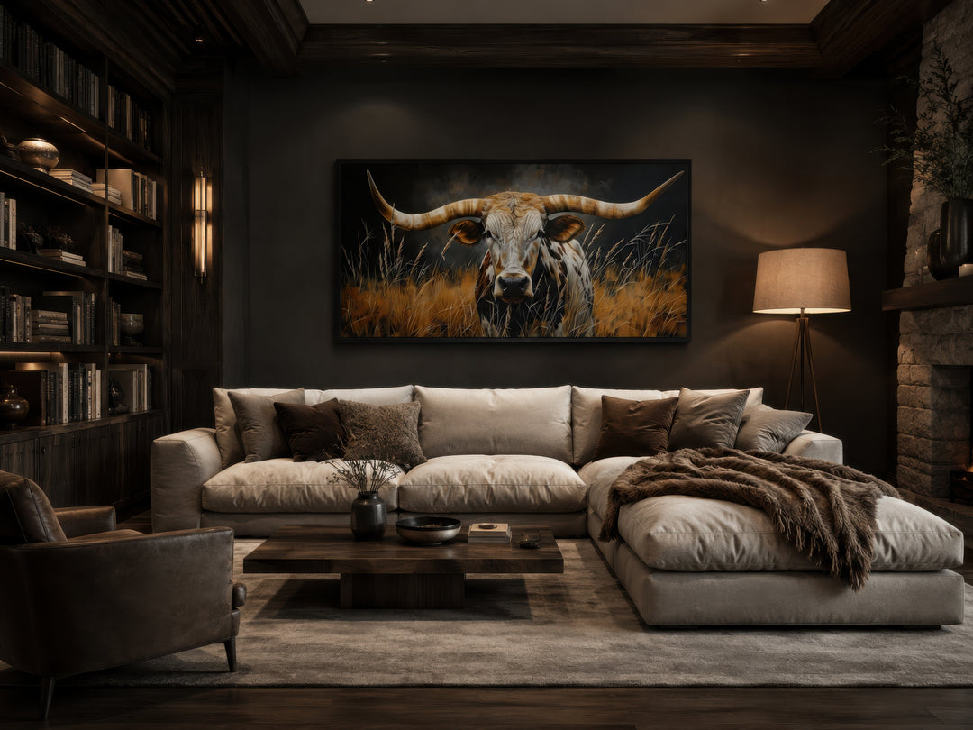 Framed canvas wall art of a Texas longhorn steer in grass, hung above a sofa in a rustic room.