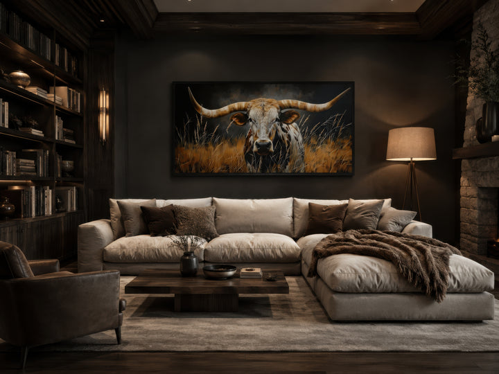 Framed canvas wall art of a Texas longhorn steer in grass, hung above a sofa in a rustic room.