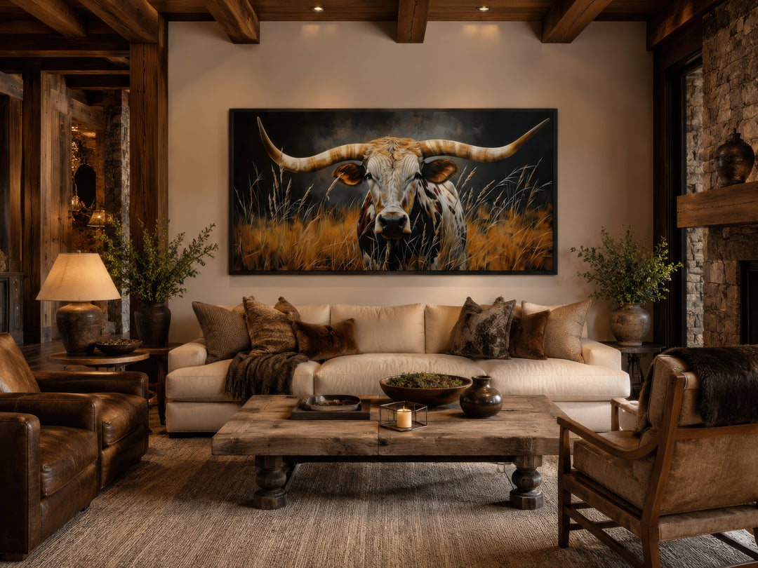 Framed canvas wall art of a Texas longhorn steer in grass above a sofa in a rustic living room.