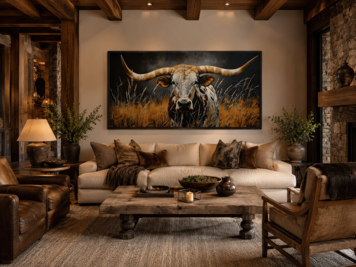 Framed canvas wall art of a Texas longhorn steer in grass above a sofa in a rustic living room.