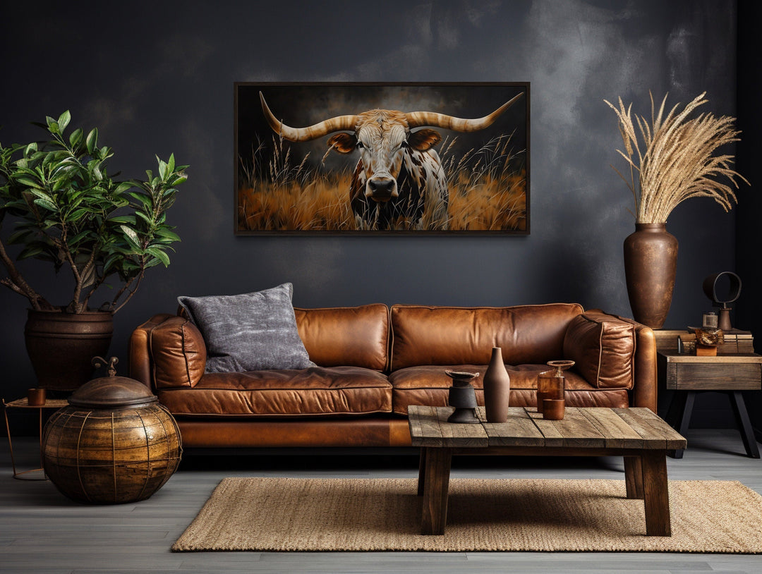Framed canvas wall art of a Texas longhorn steer in grass above a brown leather sofa.