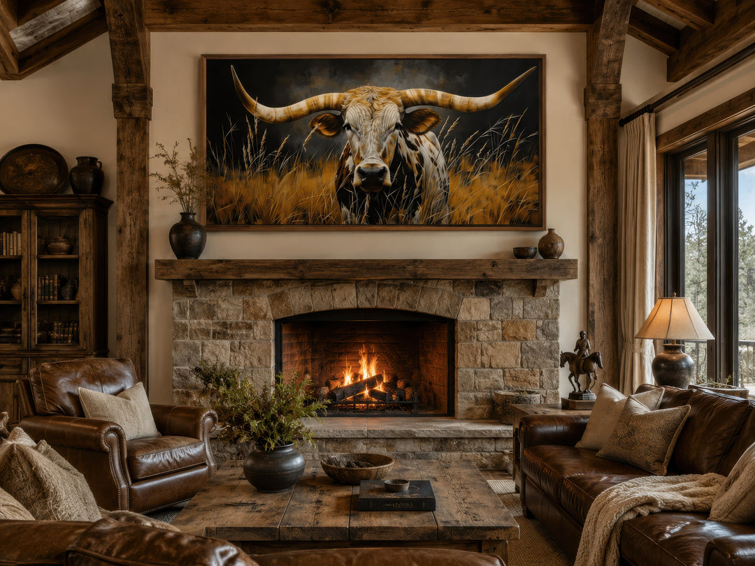 Framed canvas wall art of a Texas longhorn steer in grass above a stone fireplace in a rustic room.
