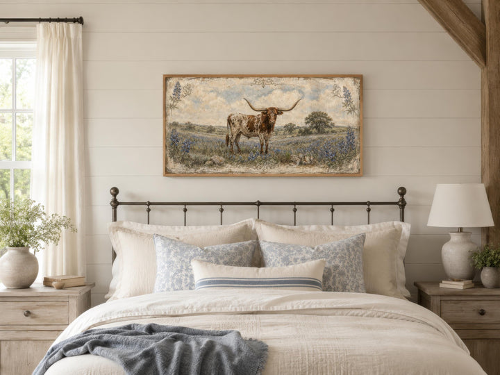 A framed canvas print of a Texas Longhorn in a bluebonnet field hangs above a rustic farmhouse bed.