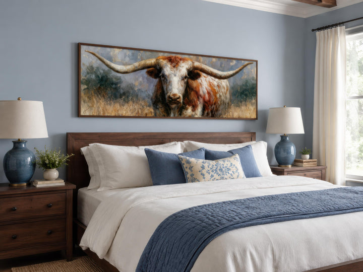 Texas Longhorn wall art canvas print in a dark wood frame hanging above a bed in a blue bedroom.