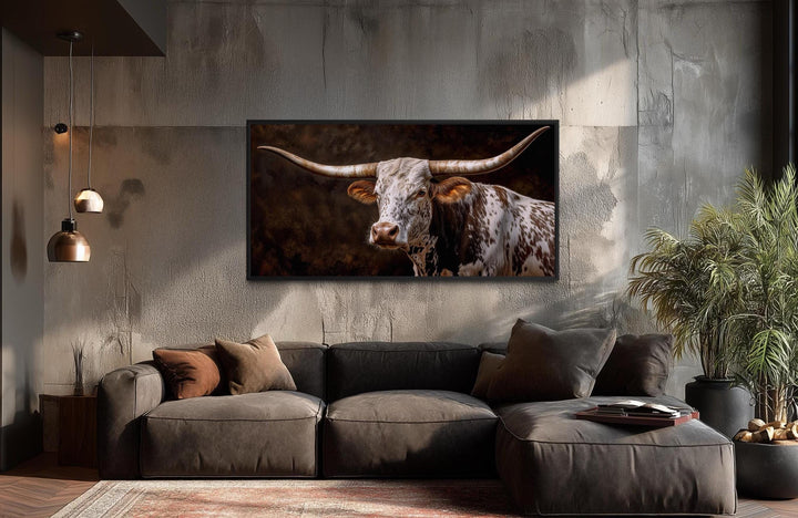A horizontal canvas print of a Texas Longhorn bull hangs above a modern sofa in a rustic room.