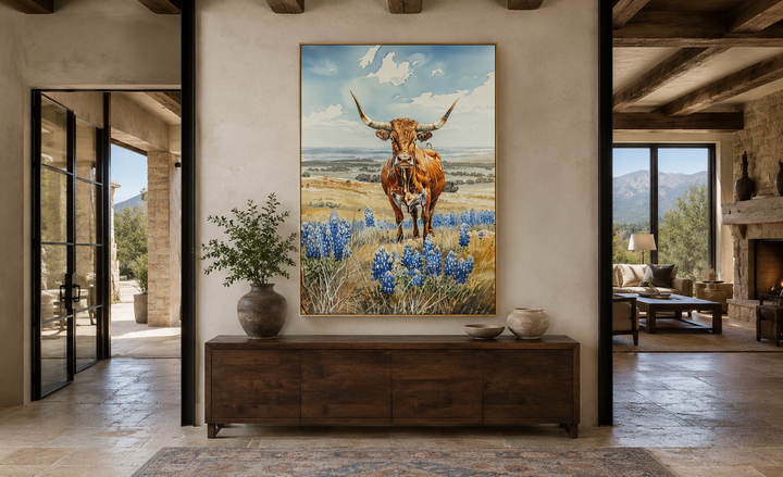 Vertical framed canvas wall art of a Texas longhorn cow in a field of bluebonnets above a sideboard.