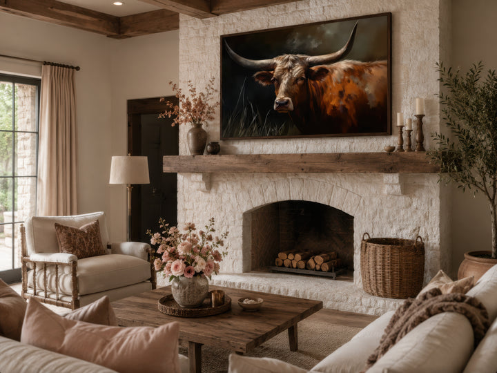 Framed canvas wall art of a Texas Longhorn cow above a rustic stone fireplace in a living room.