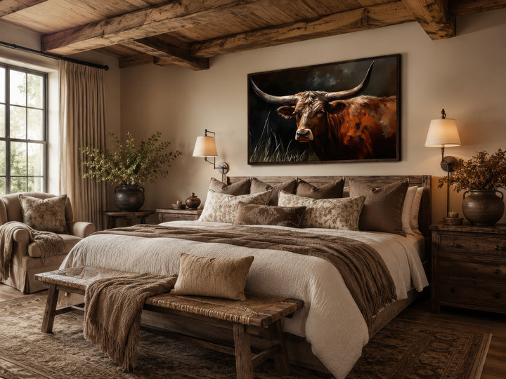 Framed canvas wall art of a Texas Longhorn cow hanging above a bed in a rustic bedroom.