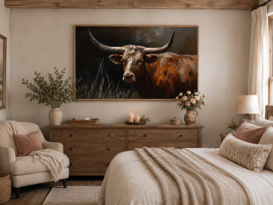 Framed canvas wall art of a brown Texas Longhorn cow hanging above a wooden dresser in a bedroom.