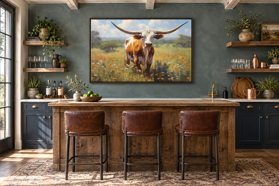 Framed canvas painting of a Texas Longhorn cow in a wildflower field above a rustic kitchen bar.