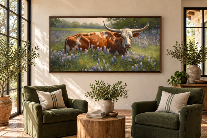 Framed canvas wall art of a Texas Longhorn cow in a field of bluebonnets above two green armchairs.
