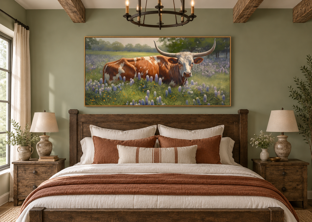 Framed canvas wall art of a Texas Longhorn cow in a field of bluebonnets above a bed.