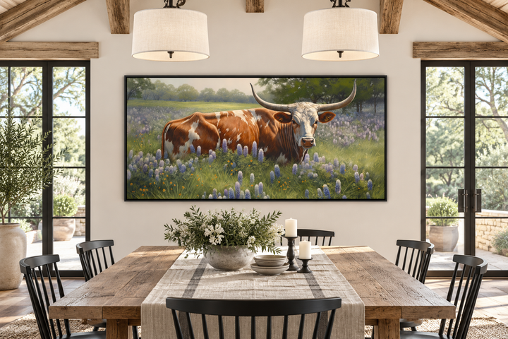 Framed canvas wall art of a Texas Longhorn cow in a field of bluebonnets above a dining table.