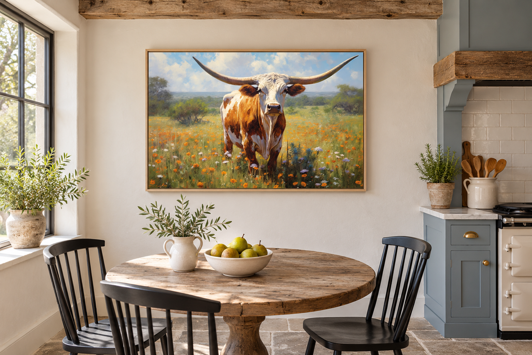 Framed canvas painting of a Texas Longhorn cow in a wildflower field above a rustic dining table.