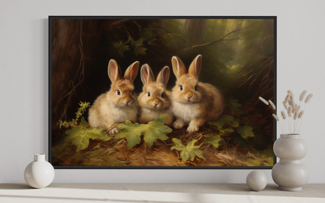 Three cute bunnies in a forest framed canvas wall art displayed above a shelf with vases.