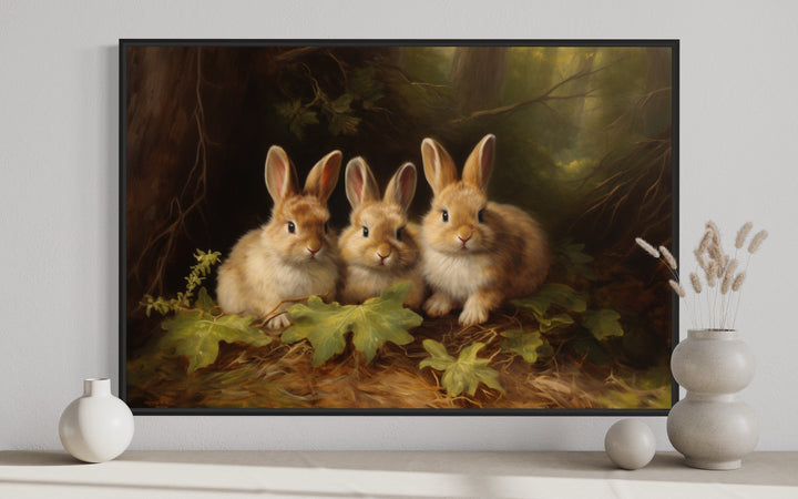 Three cute bunnies in a forest framed canvas wall art displayed above a shelf with vases.