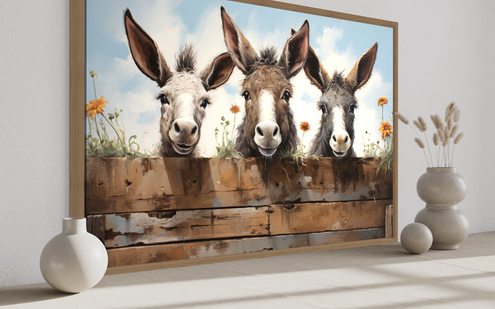 Three funny donkeys peeking over a wooden fence in a framed farmhouse wall art canvas.