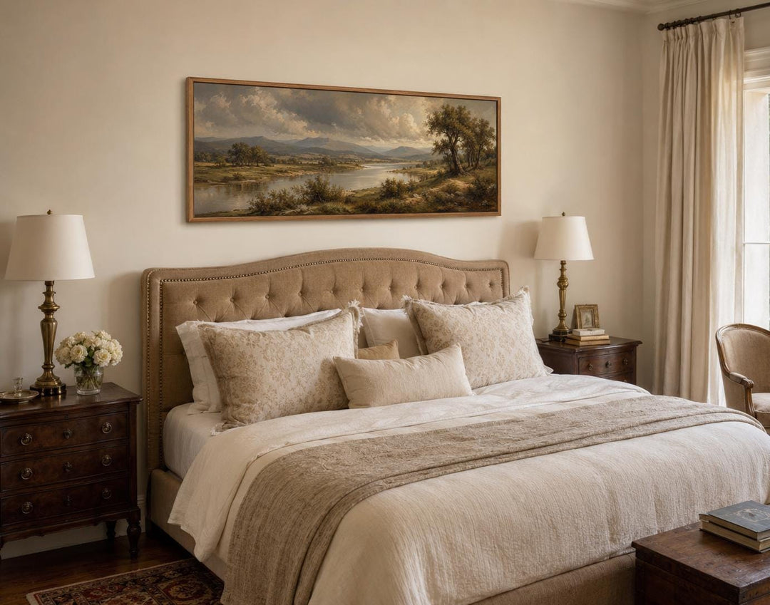 Traditional landscape canvas of a moody river valley hanging above a tufted headboard in a bedroom.