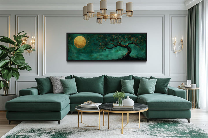 Long horizontal wall art of a golden moon and tree against an emerald green background over a sofa.