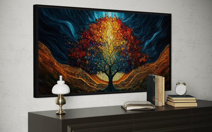 A colorful canvas print of a glowing tree of life hangs above a dark dresser with books and a lamp.