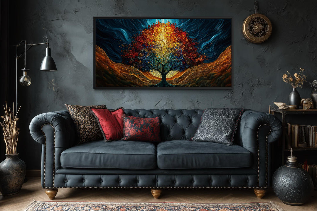 A colorful canvas print of a glowing Tree of Life hangs above a dark tufted sofa in a moody room.