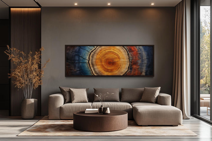 Long horizontal canvas wall art of colorful tree rings above a modern couch in a living room.