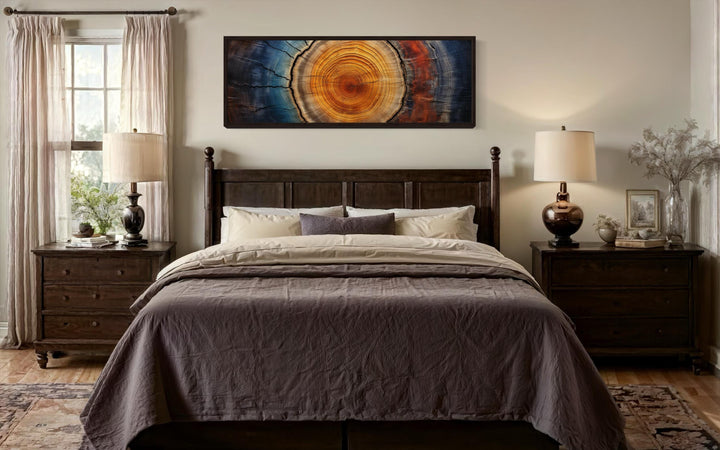 Tree ring long horizontal canvas wall art in warm and cool tones hanging above a dark wood bed.