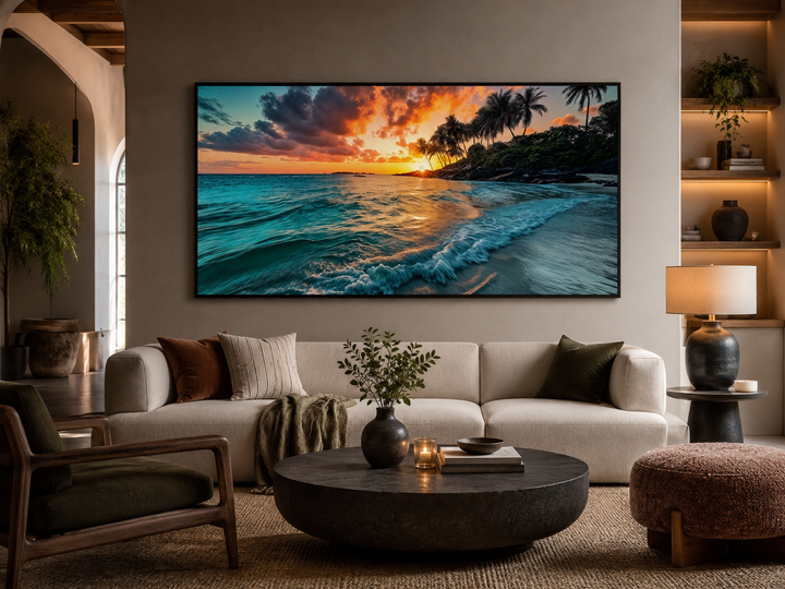Framed horizontal canvas painting of a tropical beach sunset above a modern sofa in a living room.