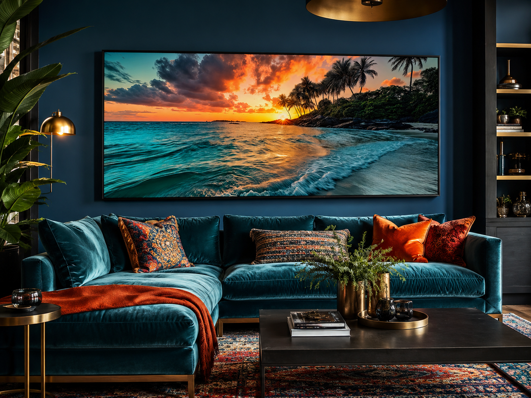 Large horizontal framed canvas painting of a tropical beach sunset above a teal velvet sofa.