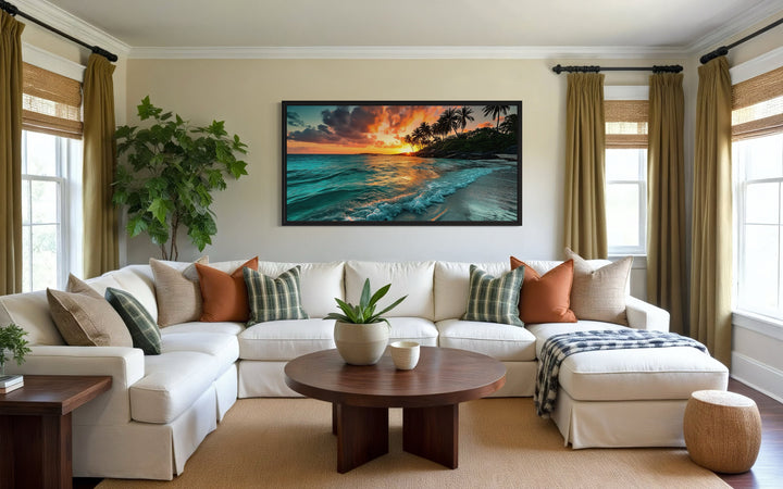 Framed canvas of a tropical beach sunset hanging above a white sectional sofa in a coastal room.