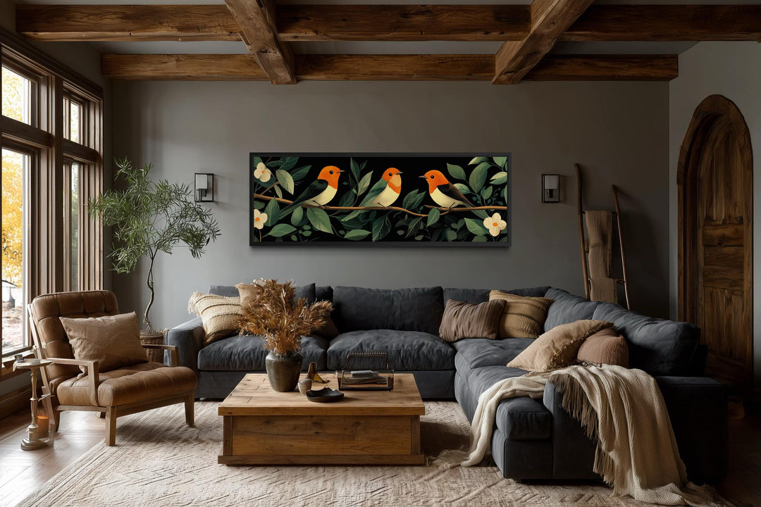 Panoramic canvas print of three orange-headed tropical birds on a branch over a dark grey sofa.