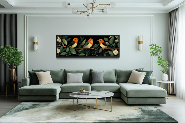 A horizontal canvas print of three colorful tropical birds perched on a branch in a modern room.