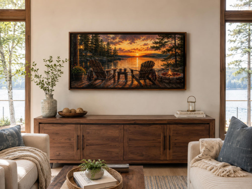 Two Adirondack chairs and a campfire by a lake at sunset framed canvas wall art in a living room.