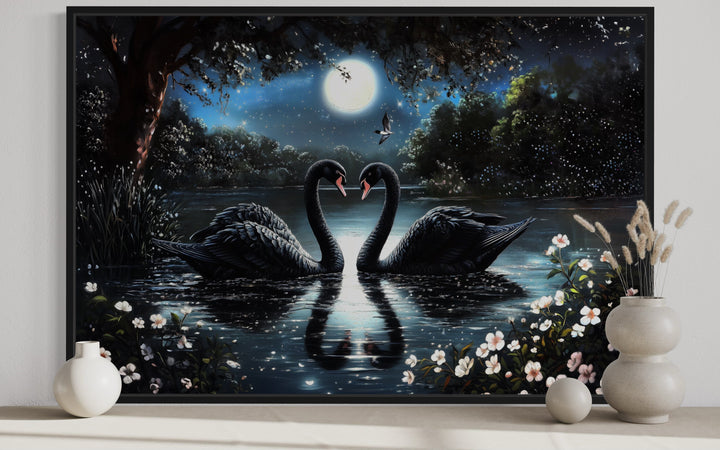 Framed canvas wall art of two black swans on a moonlit lake forming a heart shape with their necks.
