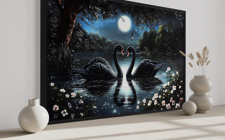 Framed canvas art of two black swans on a moonlit lake with white flowers and a full moon.