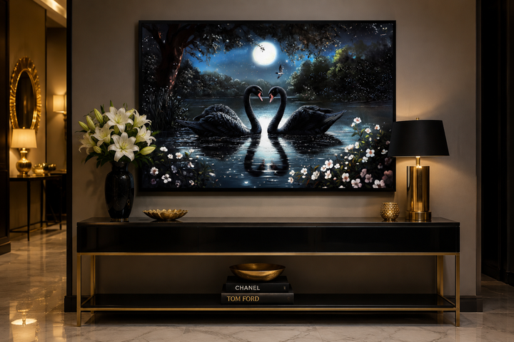 Framed canvas wall art of two black swans on a moonlit lake, displayed above a black console table.