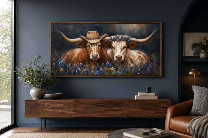 Framed canvas art of two Texas longhorns with cowboy hats and bluebonnets above a wooden sideboard.