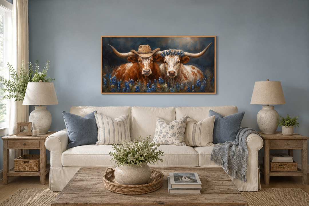 Two Texas longhorns wall art with cowboy hats and bluebonnets above a cream sofa in a rustic room.