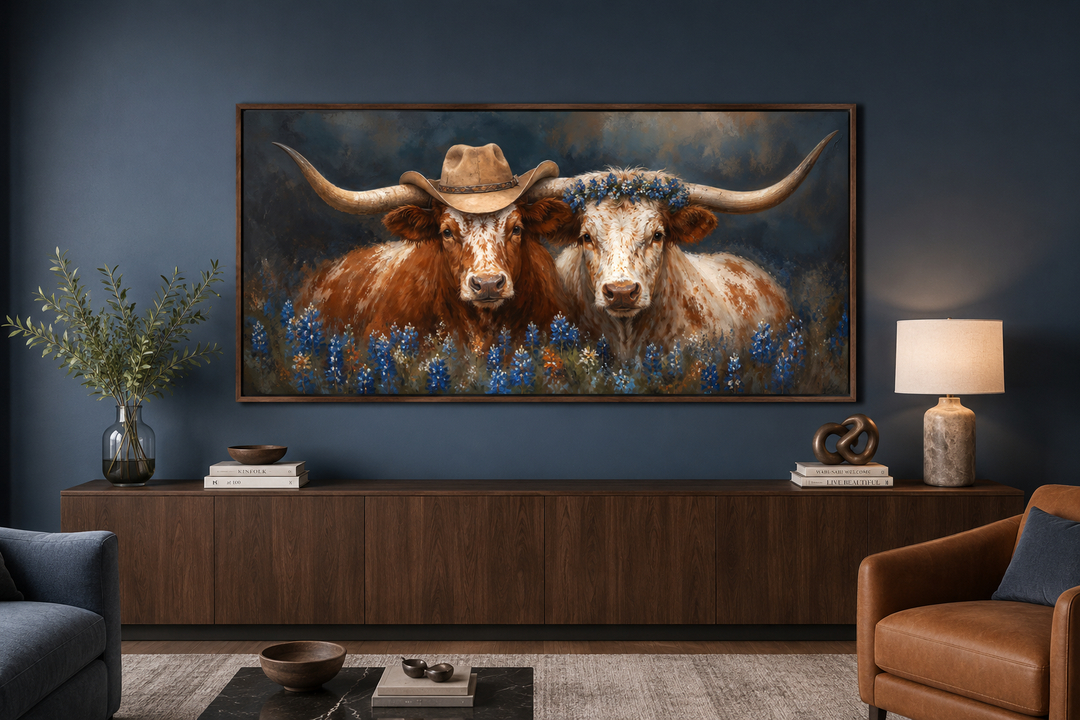 Framed canvas art of two Texas longhorns with cowboy hats and bluebonnets over a dark wood sideboard.