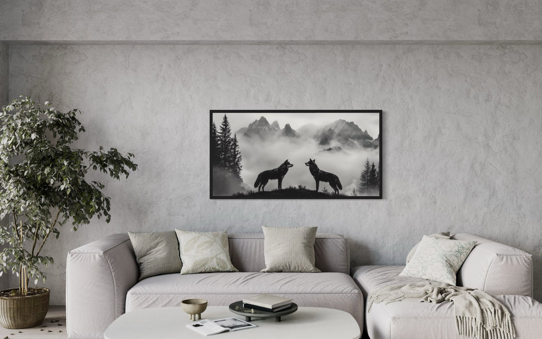 Black and white framed canvas wall art of two wolves on a cliff in foggy mountains above a sofa.