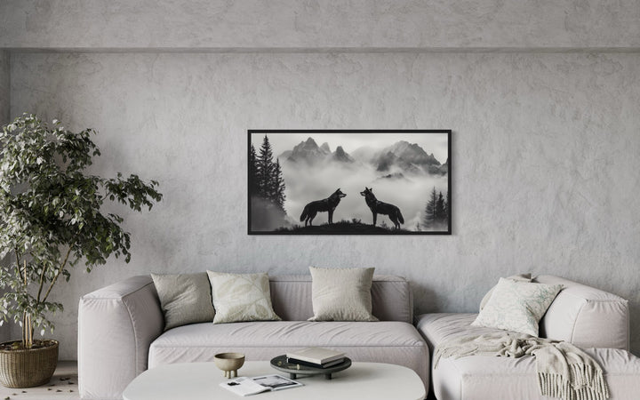 Black and white framed canvas wall art of two wolves on a cliff in foggy mountains above a sofa.