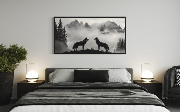 Two wolves on a cliff in foggy mountains black and white framed canvas art above a bed.
