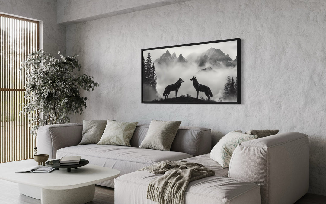 Two wolves on a cliff in foggy mountains black and white framed canvas wall art in a living room.