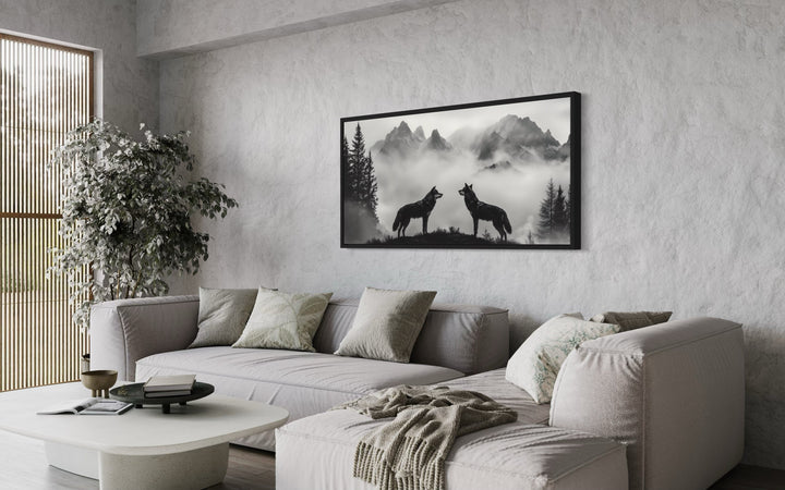 Two wolves on a cliff in foggy mountains black and white framed canvas wall art in a living room.
