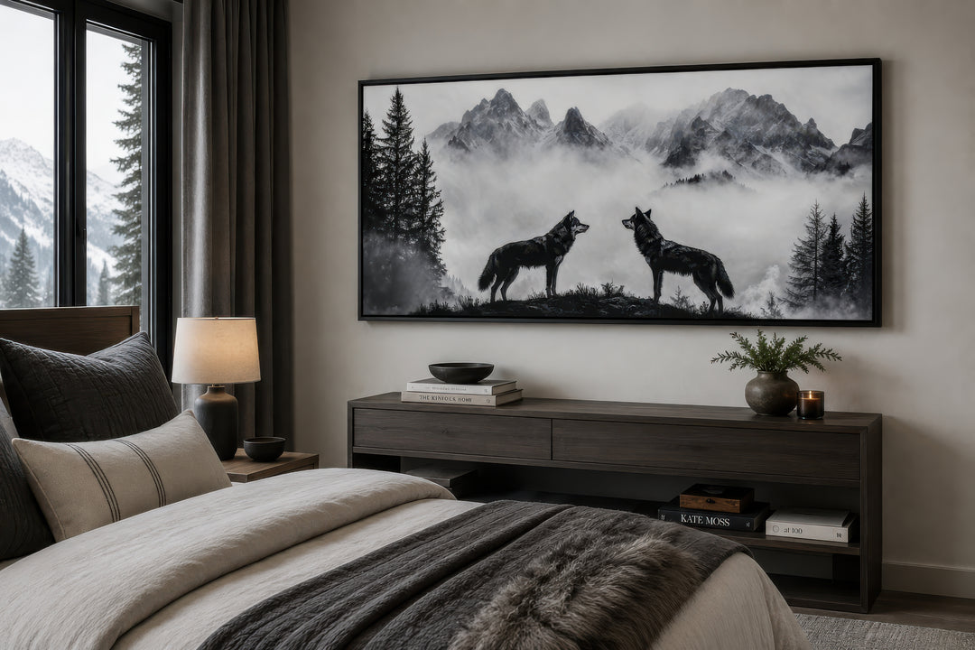 Black and white framed canvas art of two wolves on a cliff in foggy mountains above a bedroom bed.