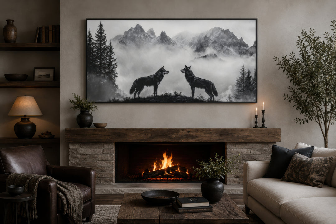 Black and white framed canvas art of two wolves on a cliff in foggy mountains above a fireplace.